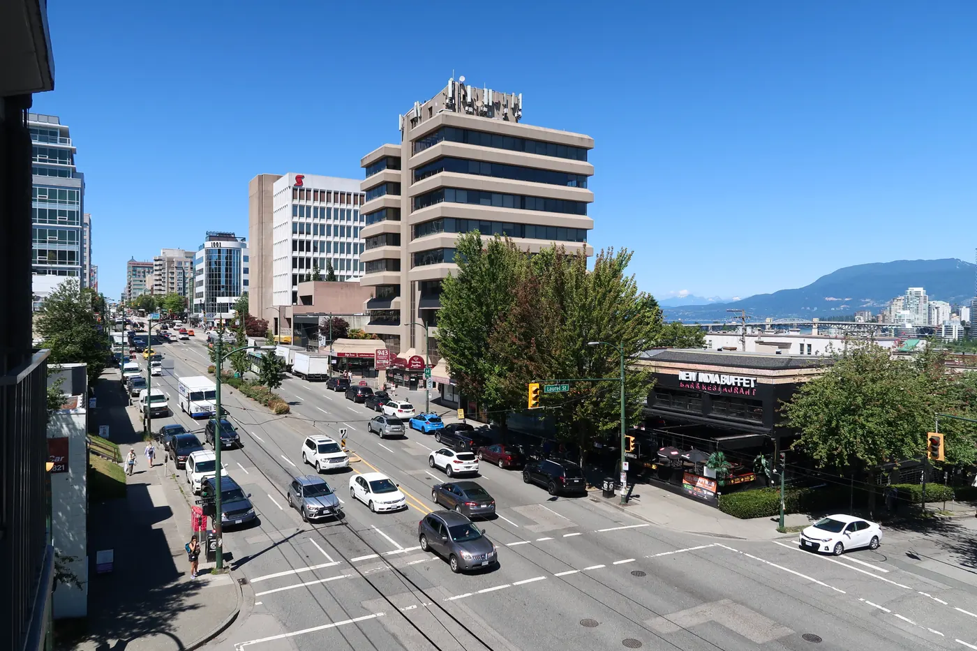 Traffic on West Broadway in Vancouver with mid-rise office buildings and mountains in the distance